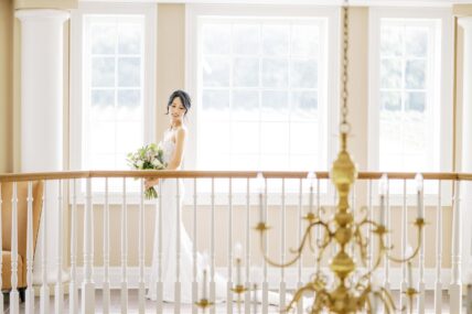 A bride holding a flower bouquet in an indoor wedding venue.